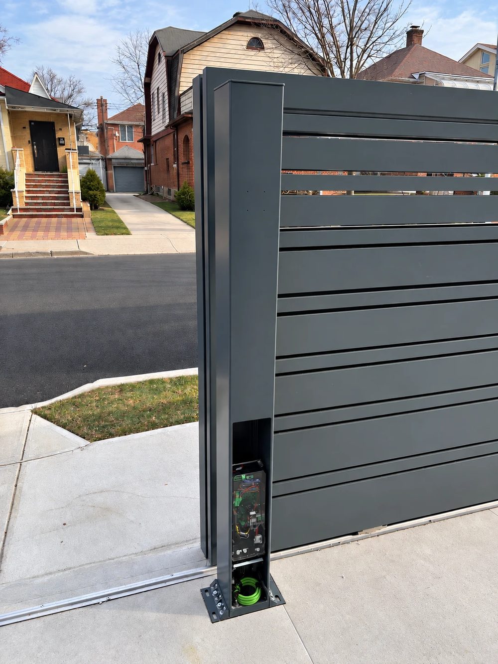 The sliding gate's operator housed inside the gate post, its cover open at the base