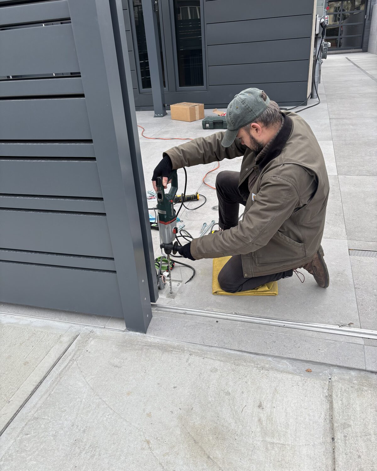 Fortis technician drilling a post anchor beside a new slat fence panel